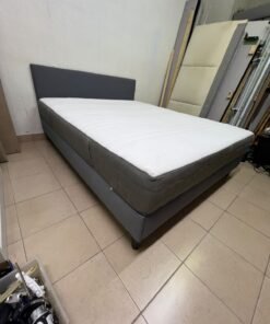 A gray upholstered bed frame with a white mattress and blanket, or a dark gray mattress on the side.