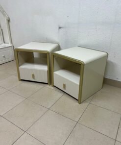 The image shows two modern bedside tables in a creamy white finish, featuring gold frames and details, as well as ribbed drawer fronts (from Home Centre). - Image 2