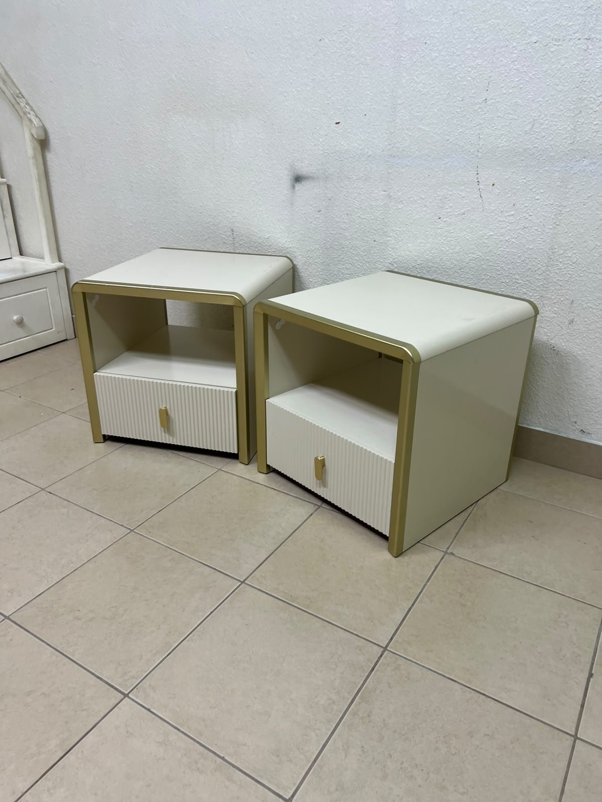 The image shows two modern bedside tables in a creamy white finish, featuring gold frames and details, as well as ribbed drawer fronts (from Home Centre). - Image 2