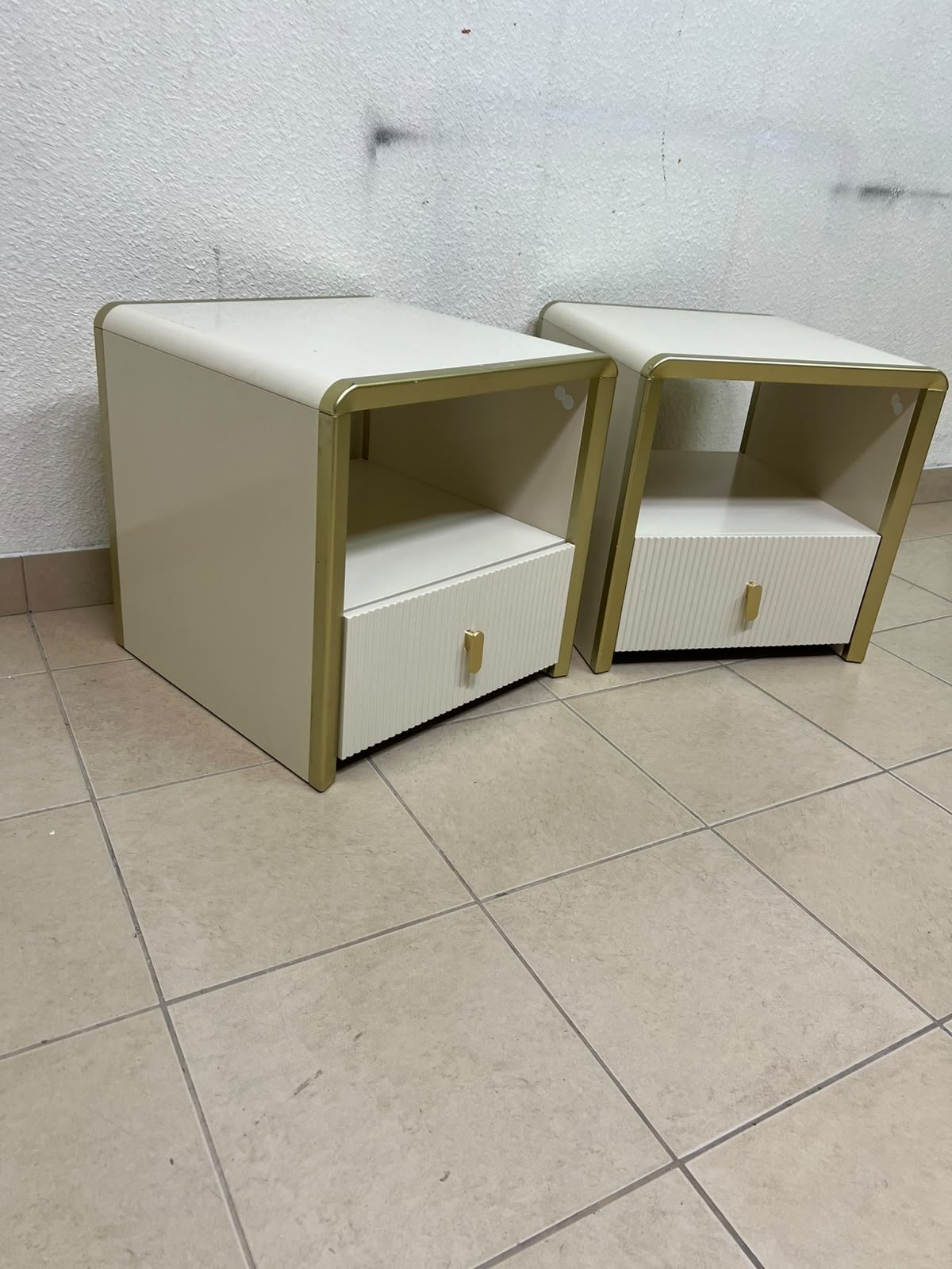 The image shows two modern bedside tables in a creamy white finish, featuring gold frames and details, as well as ribbed drawer fronts (from Home Centre). - Image 3