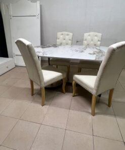 An oval dining table with a marble-patterned ceramic top, surrounded by four chairs upholstered in light beige fabric and featuring button-tufted backrests.