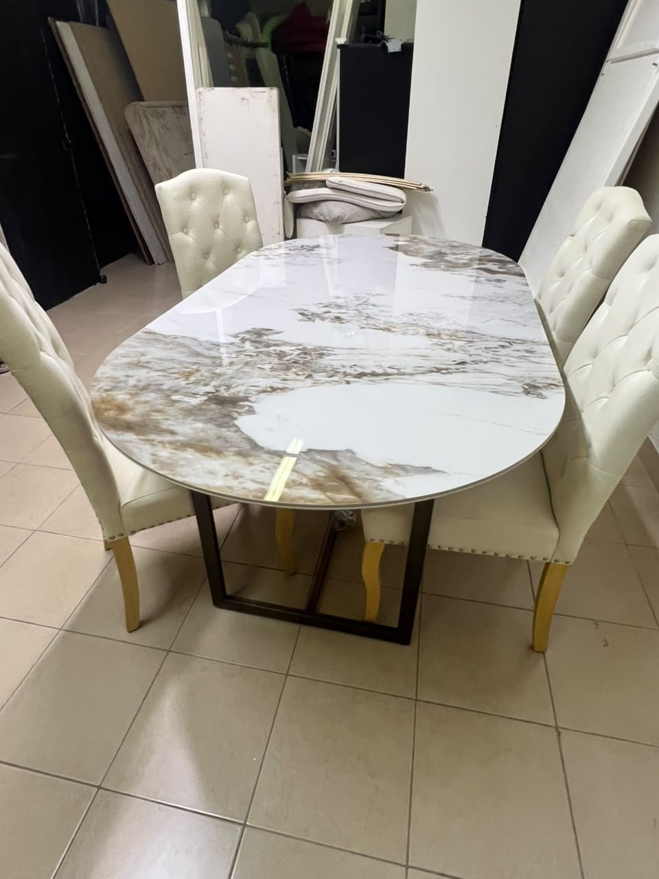 An oval dining table with a marble-patterned ceramic top, surrounded by four chairs upholstered in light beige fabric and featuring button-tufted backrests. - Image 11