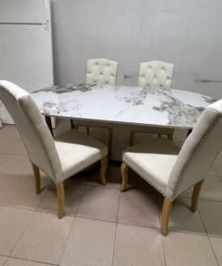 An oval dining table with a marble-patterned ceramic top, surrounded by four chairs upholstered in light beige fabric and featuring button-tufted backrests. - Image 2