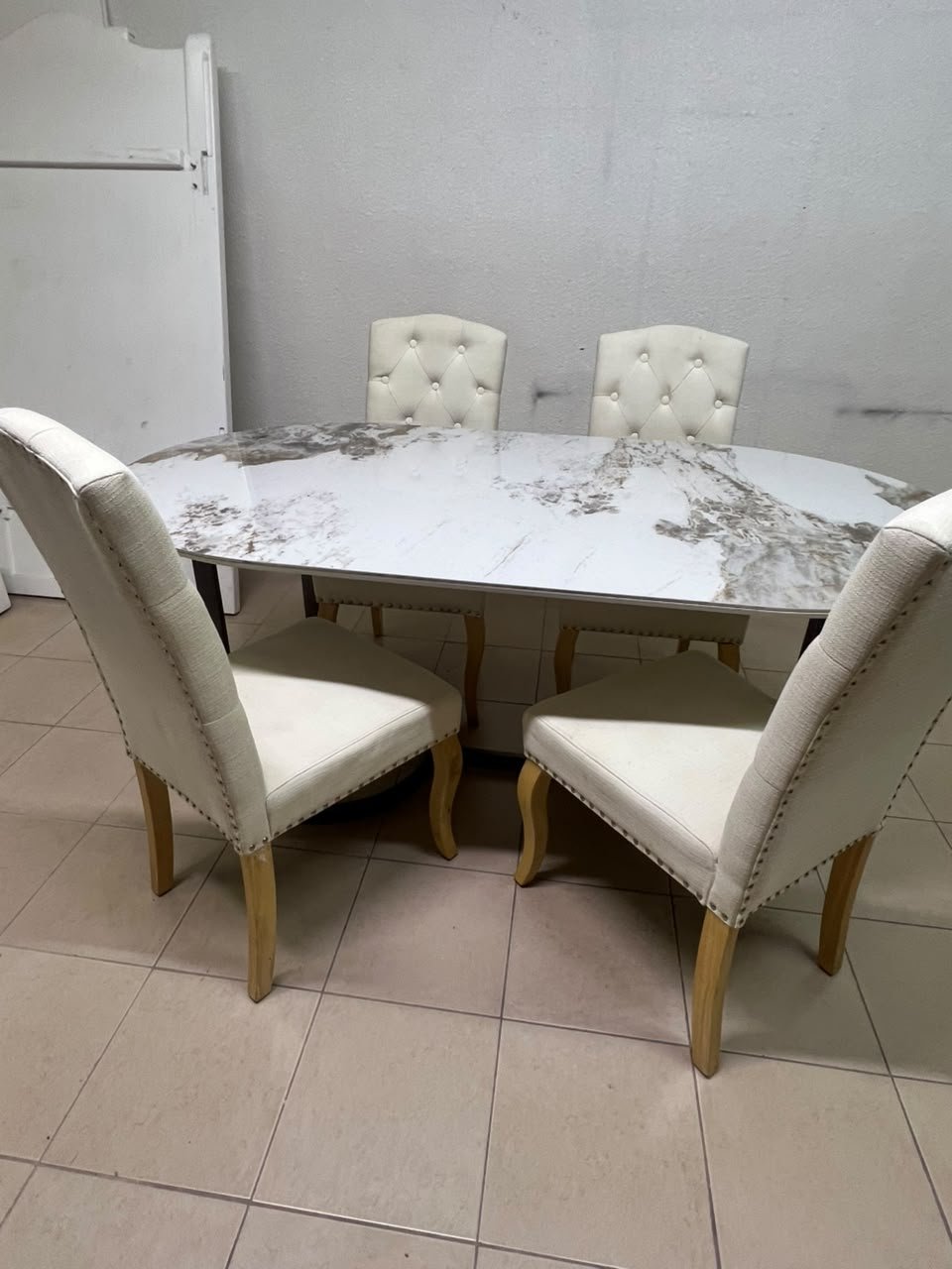 An oval dining table with a marble-patterned ceramic top, surrounded by four chairs upholstered in light beige fabric and featuring button-tufted backrests. - Image 2