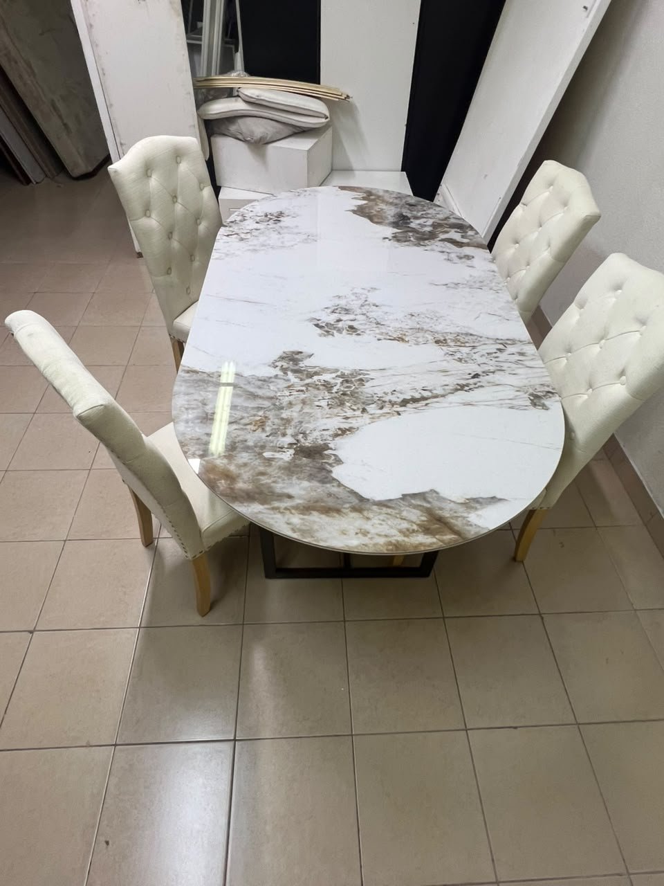 An oval dining table with a marble-patterned ceramic top, surrounded by four chairs upholstered in light beige fabric and featuring button-tufted backrests. - Image 3