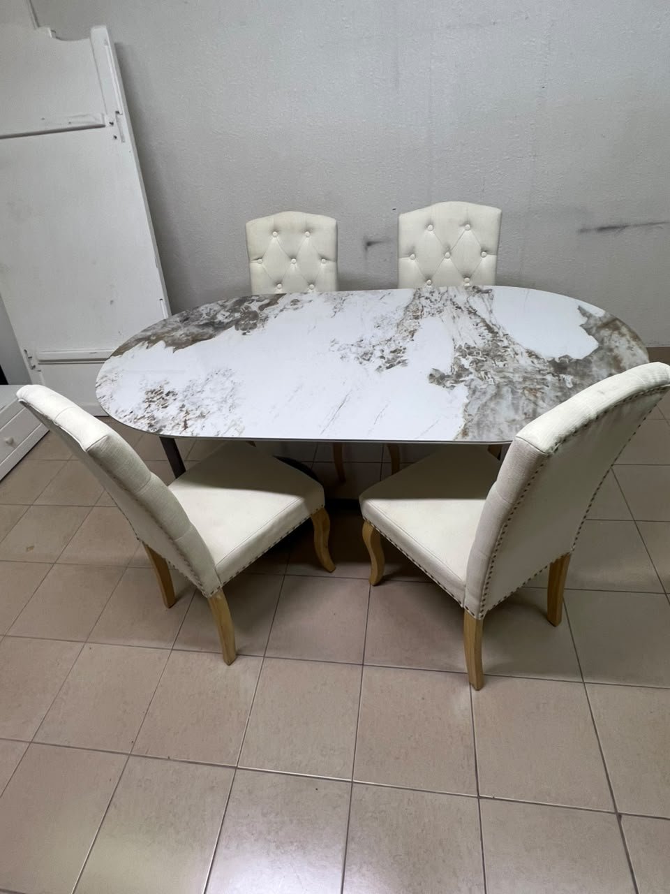 An oval dining table with a marble-patterned ceramic top, surrounded by four chairs upholstered in light beige fabric and featuring button-tufted backrests. - Image 5