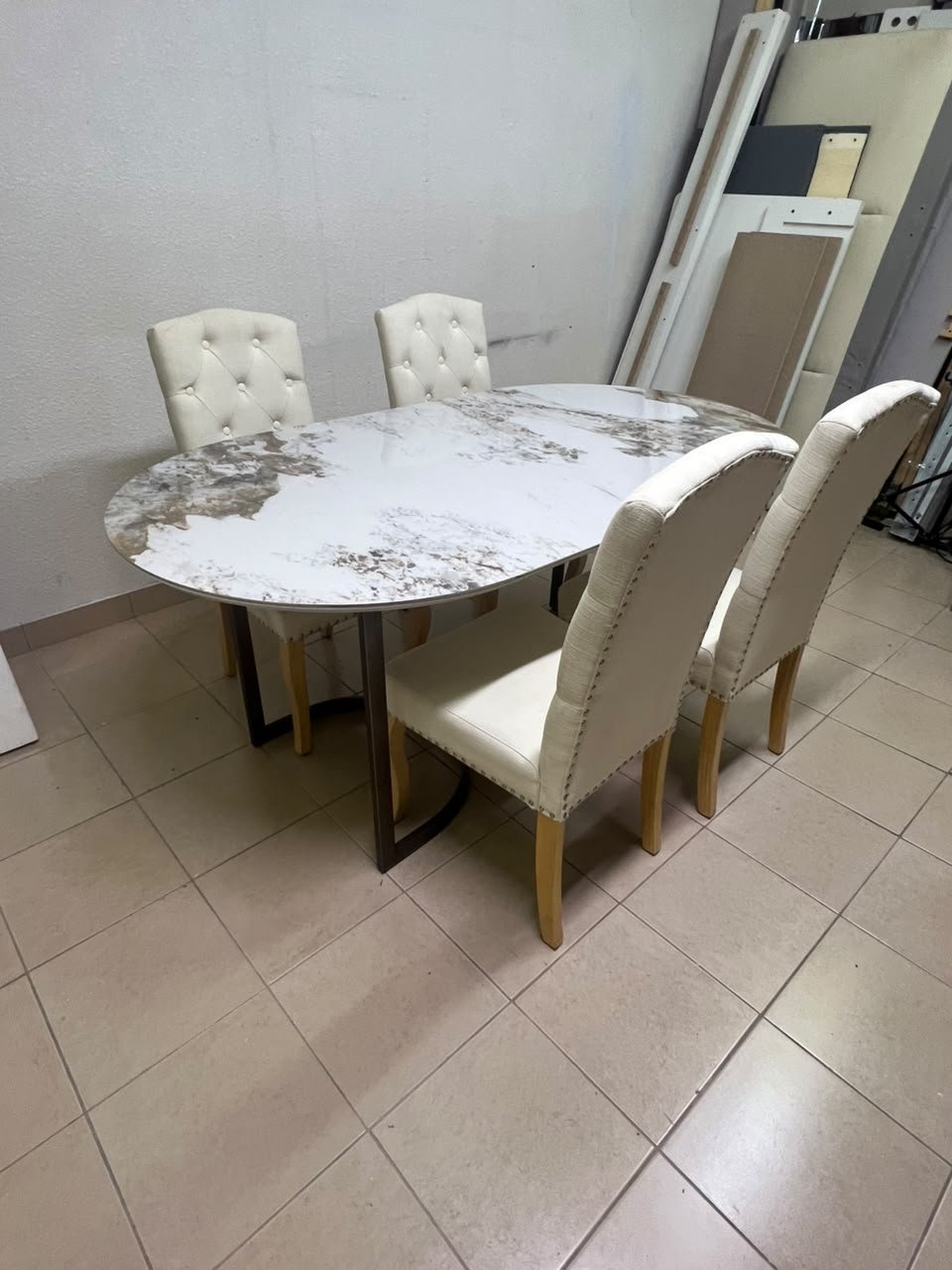An oval dining table with a marble-patterned ceramic top, surrounded by four chairs upholstered in light beige fabric and featuring button-tufted backrests. - Image 8