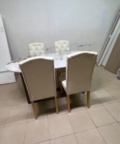 An oval dining table with a marble-patterned ceramic top, surrounded by four chairs upholstered in light beige fabric and featuring button-tufted backrests. - Image 10