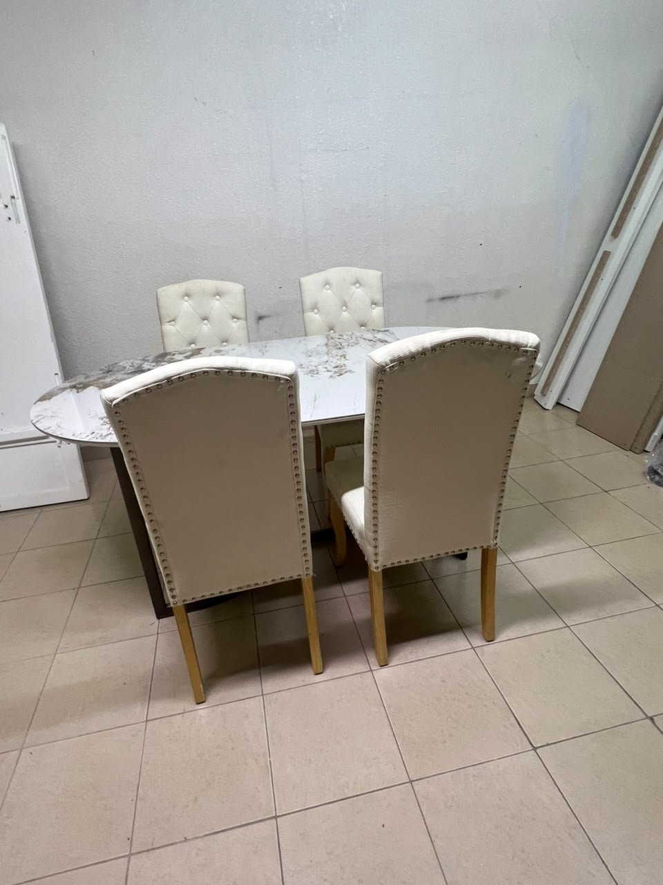 An oval dining table with a marble-patterned ceramic top, surrounded by four chairs upholstered in light beige fabric and featuring button-tufted backrests. - Image 10