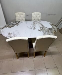 An oval dining table with a marble-patterned ceramic top, surrounded by four chairs upholstered in light beige fabric and featuring button-tufted backrests. - Image 13