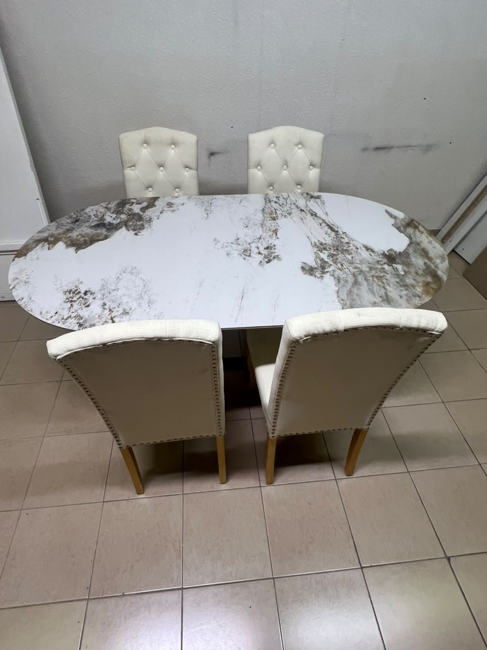 An oval dining table with a marble-patterned ceramic top, surrounded by four chairs upholstered in light beige fabric and featuring button-tufted backrests. - Image 13