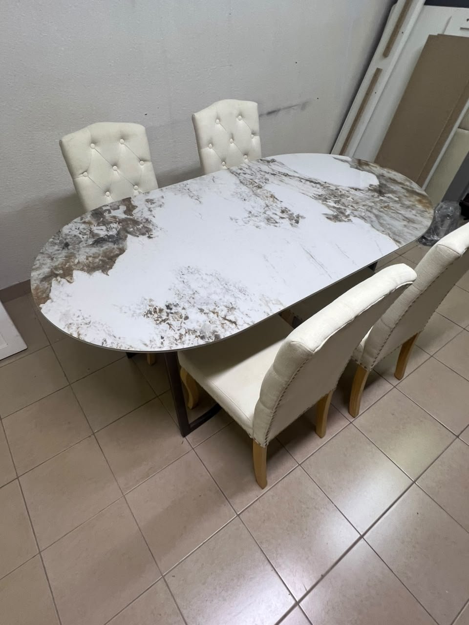 An oval dining table with a marble-patterned ceramic top, surrounded by four chairs upholstered in light beige fabric and featuring button-tufted backrests. - Image 14