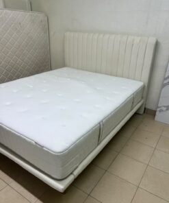 An upholstered double bed in white or light beige with a striped headboard, featuring a comfortable white mattress – Home Centre.
