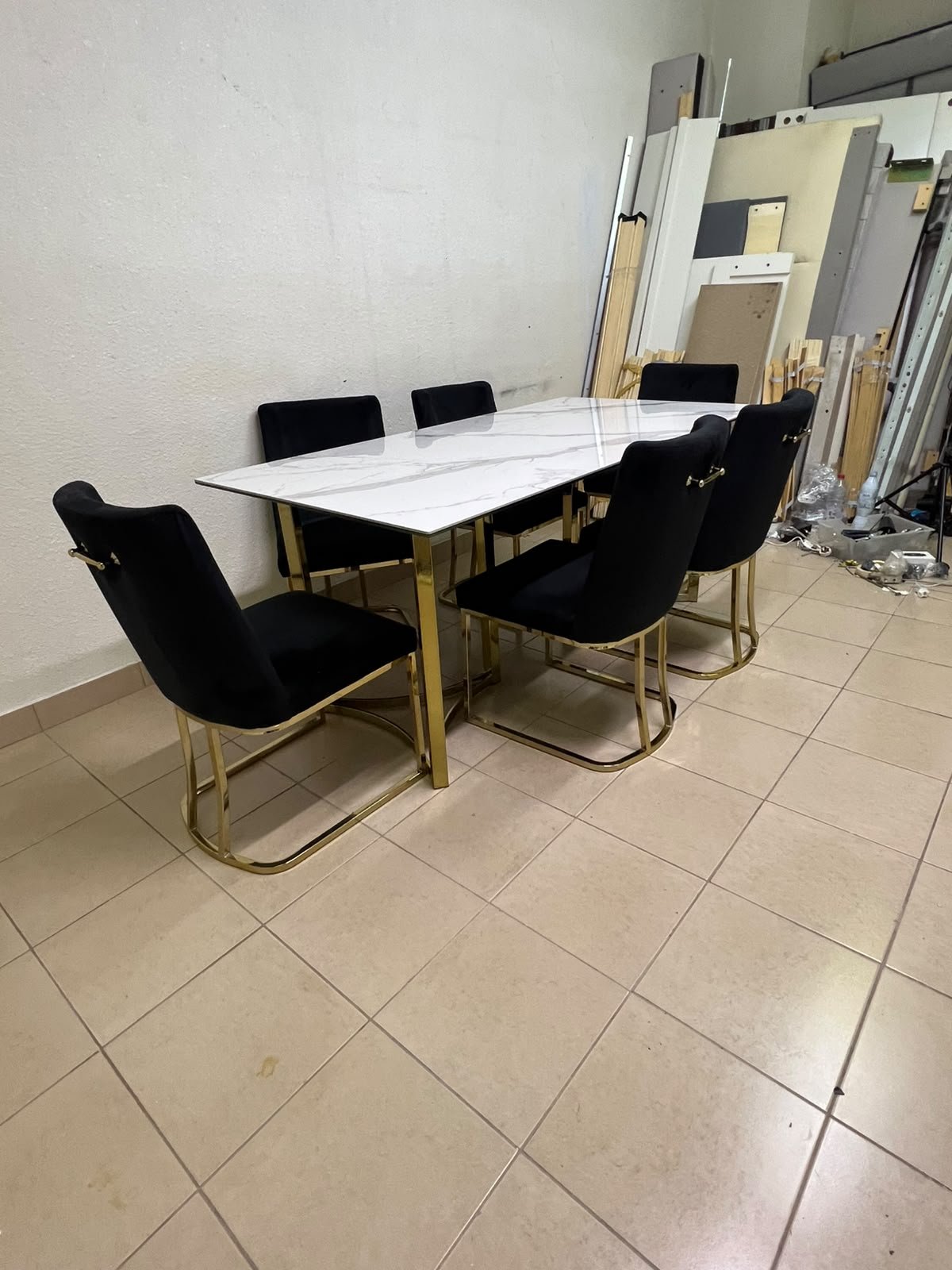 A modern six-seater dining set featuring an elegant design that combines a white marble-patterned tabletop with a gold metal base and frame, paired with black velvet chairs featuring matching gold legs.