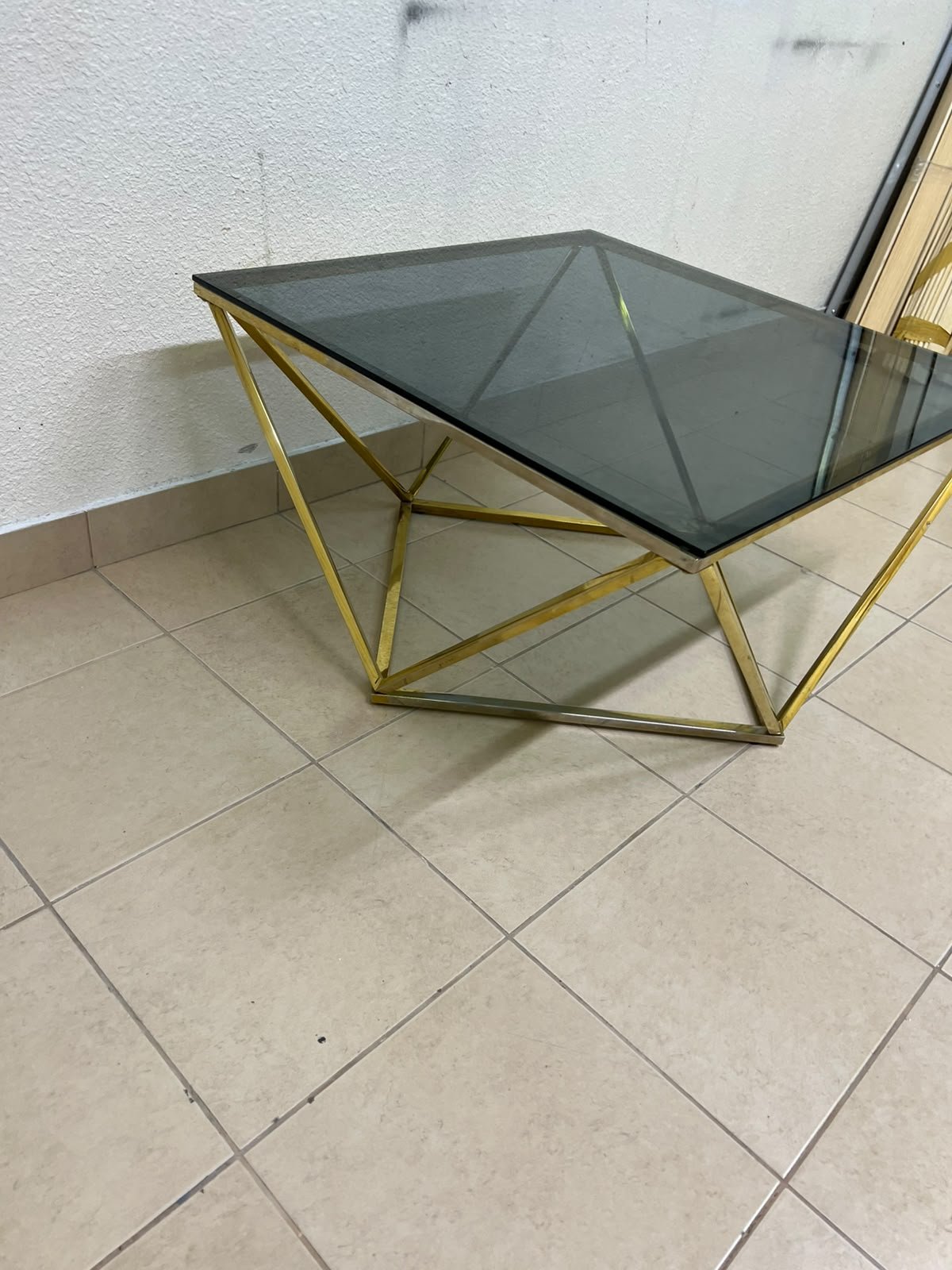 A modern, square coffee table featuring a dark or smoked glass top and a cohesive, diamond-inspired geometric base made of metal or polished gold-tone steel. - Image 2