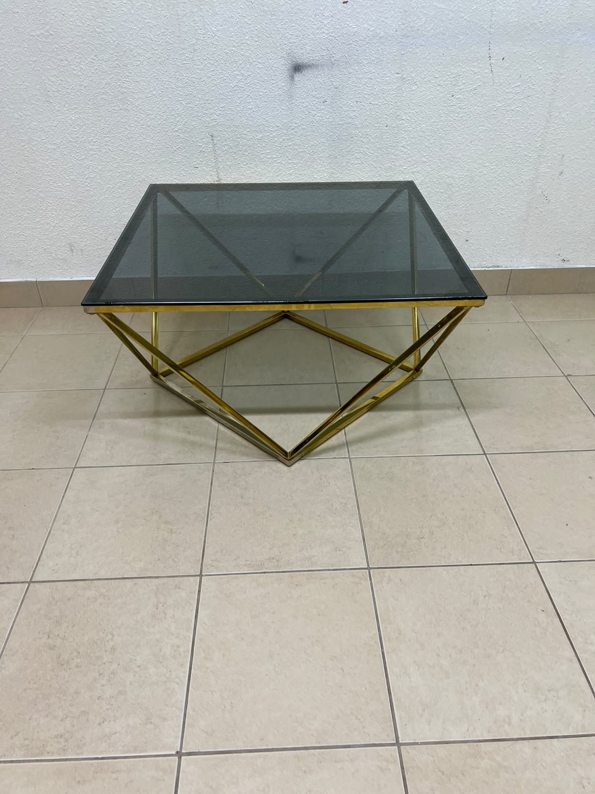 A modern, square coffee table featuring a dark or smoked glass top and a cohesive, diamond-inspired geometric base made of metal or polished gold-tone steel. - Image 3