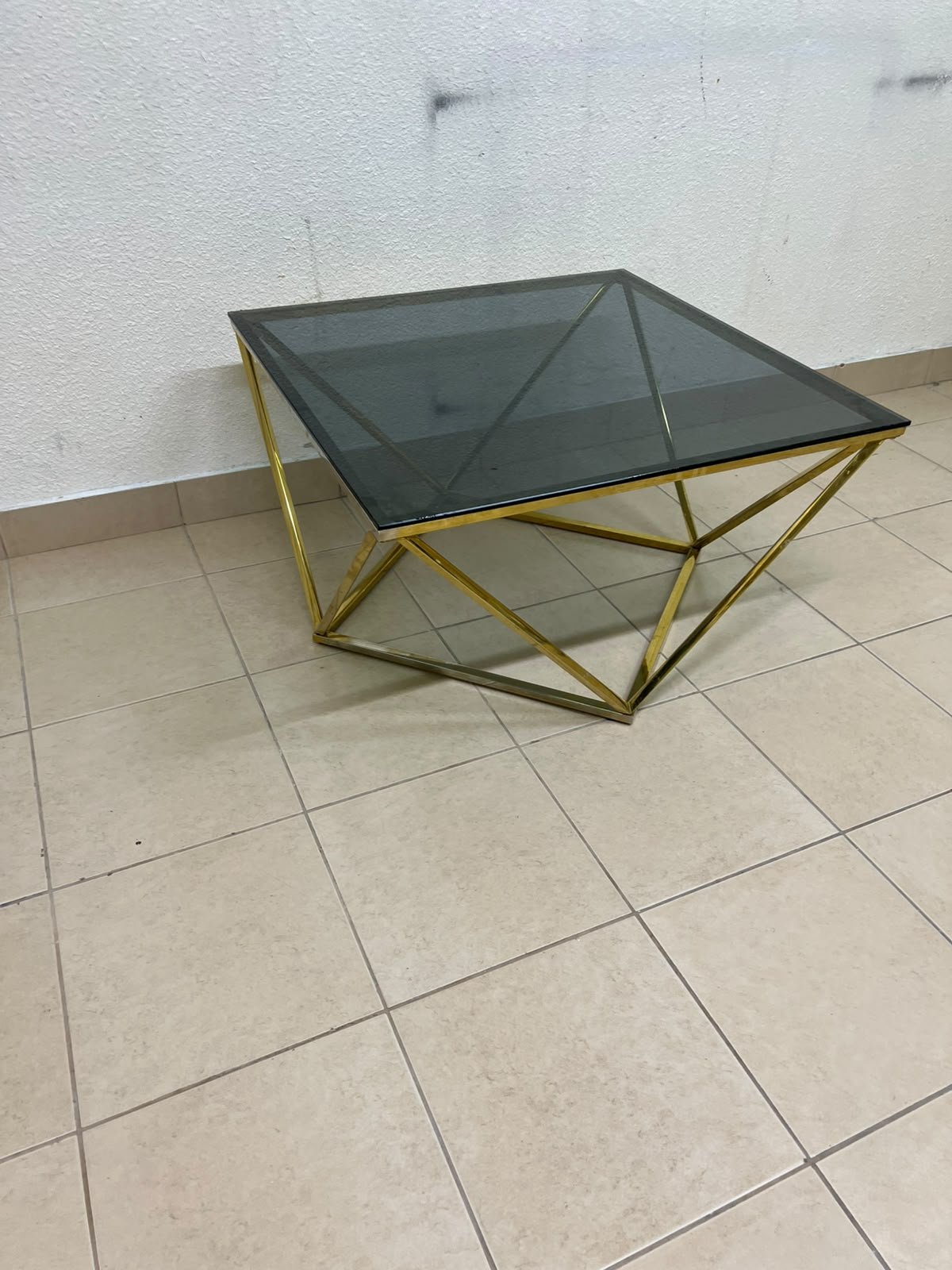 A modern, square coffee table featuring a dark or smoked glass top and a cohesive, diamond-inspired geometric base made of metal or polished gold-tone steel. - Image 4