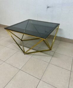 A modern, square coffee table featuring a dark or smoked glass top and a cohesive, diamond-inspired geometric base made of metal or polished gold-tone steel.
