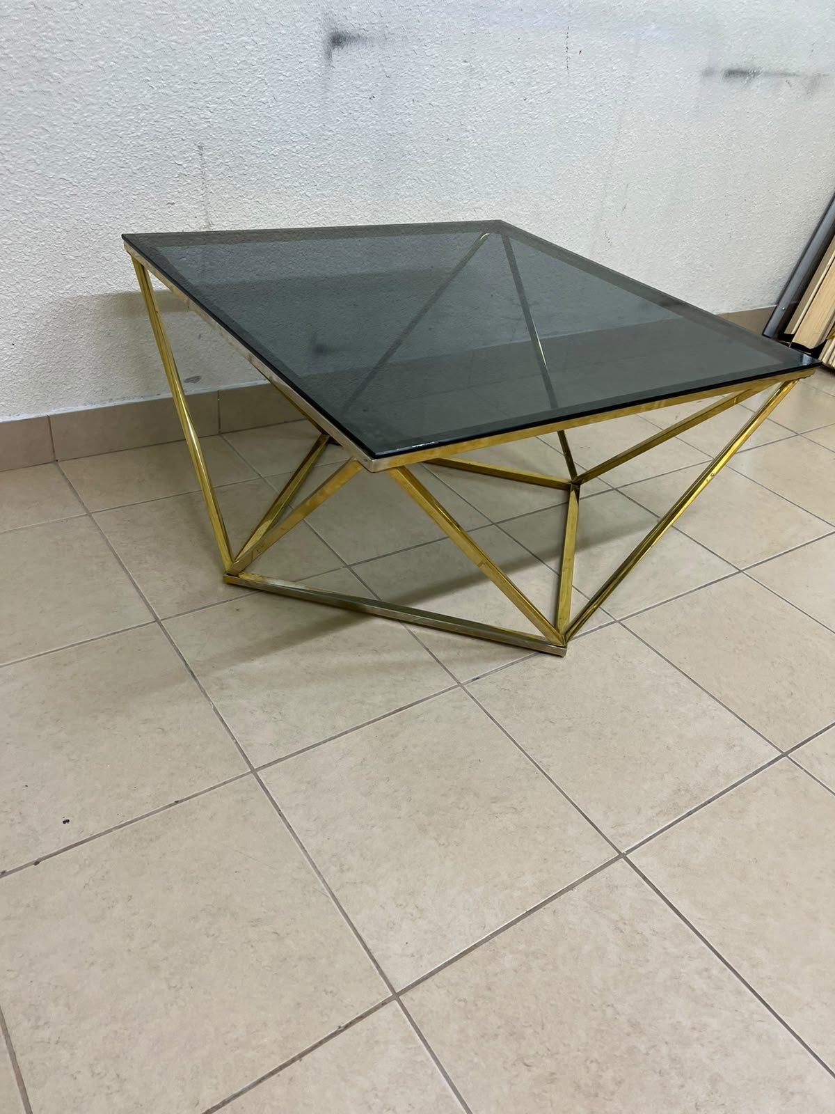 A modern, square coffee table featuring a dark or smoked glass top and a cohesive, diamond-inspired geometric base made of metal or polished gold-tone steel. - Image 8