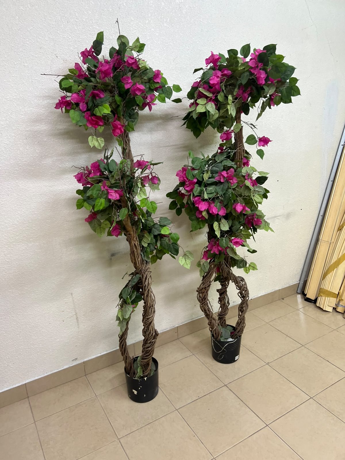 An artificial Bougainvillea tree featuring attractive pink blossoms and green foliage, distinguished by natural, expertly braided wooden trunks and set in black plastic pots. - Image 7