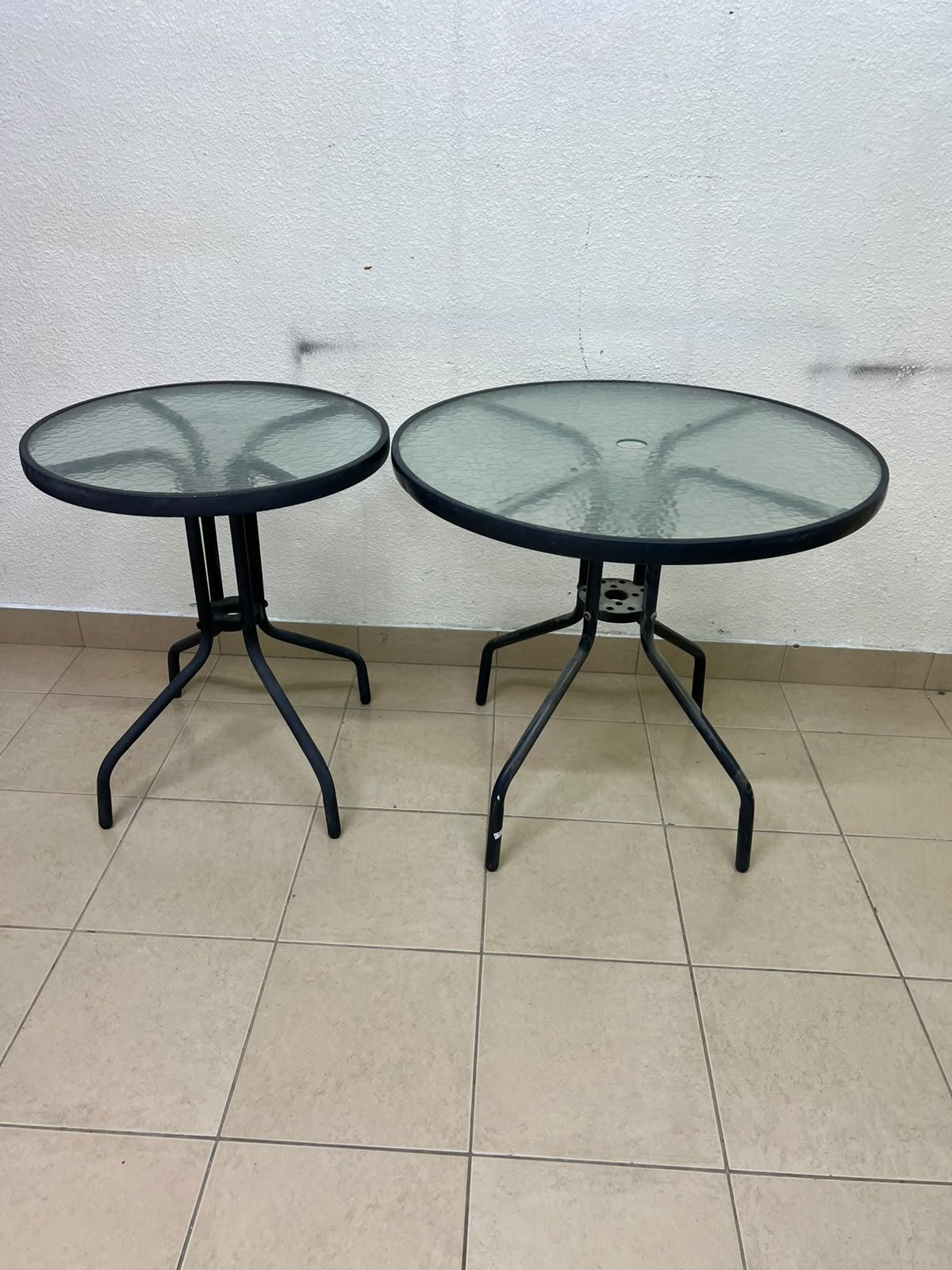 A round garden table featuring a black metal frame and a tempered glass top, suitable for outdoor use on balconies or in gardens.