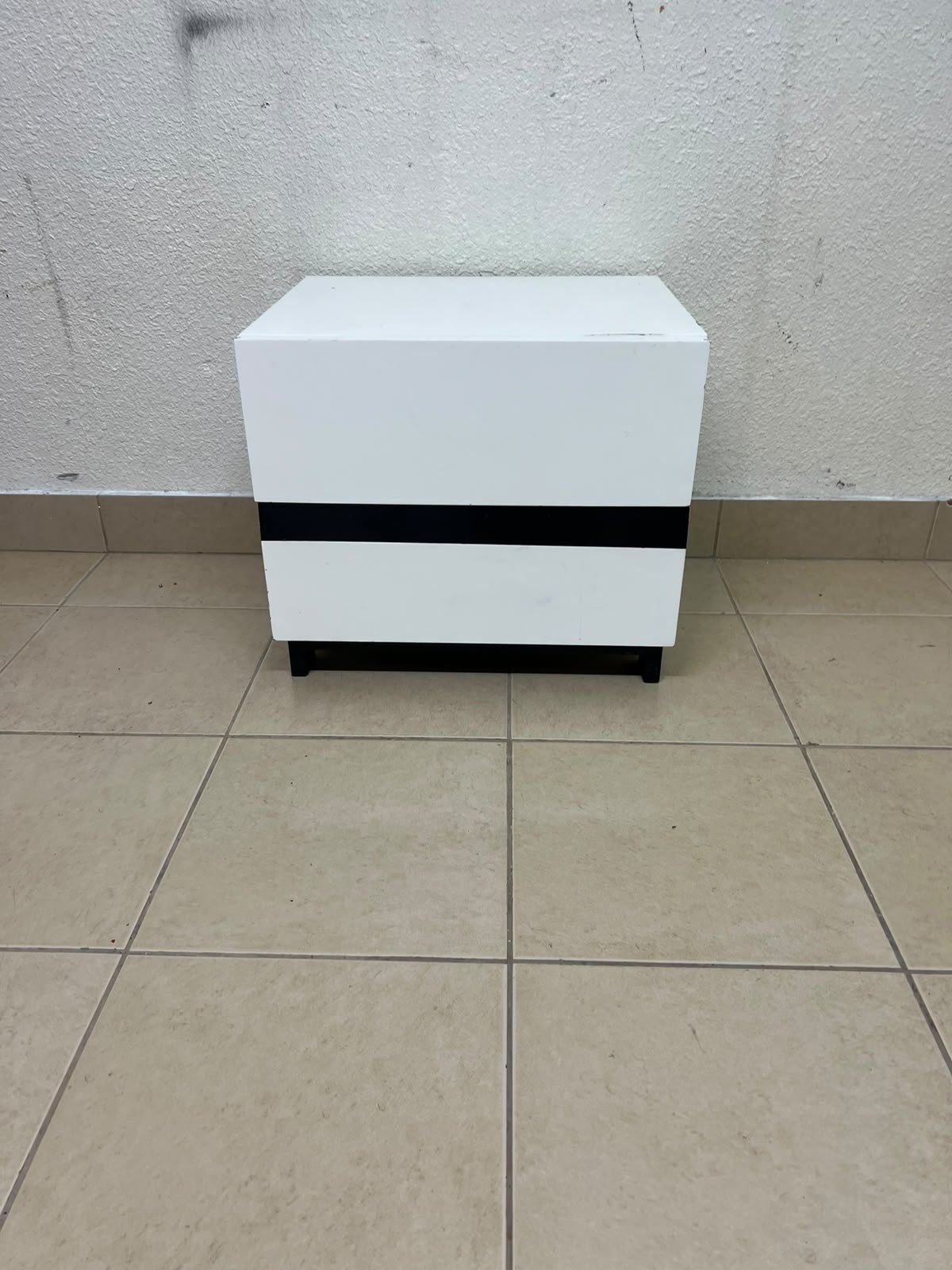 A modern-design bedside table (nightstand) made of engineered wood in white, featuring contrasting black lines.
