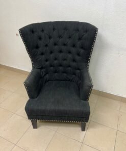 A single upholstered wingback chair featuring a button-tufted back, a black or dark gray fabric finish, and metal nailhead trim along the edges. - Image 2