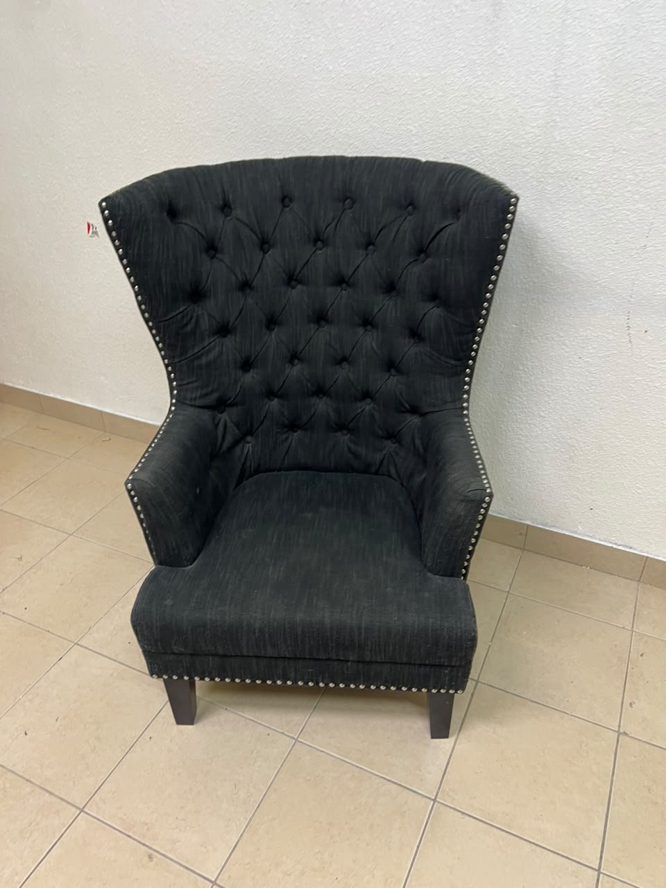 A single upholstered wingback chair featuring a button-tufted back, a black or dark gray fabric finish, and metal nailhead trim along the edges. - Image 2