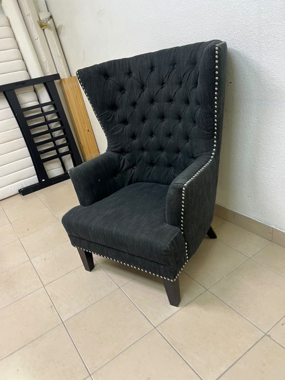 A single upholstered wingback chair featuring a button-tufted back, a black or dark gray fabric finish, and metal nailhead trim along the edges. - Image 4
