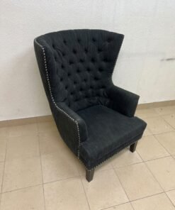 A single upholstered wingback chair featuring a button-tufted back, a black or dark gray fabric finish, and metal nailhead trim along the edges.