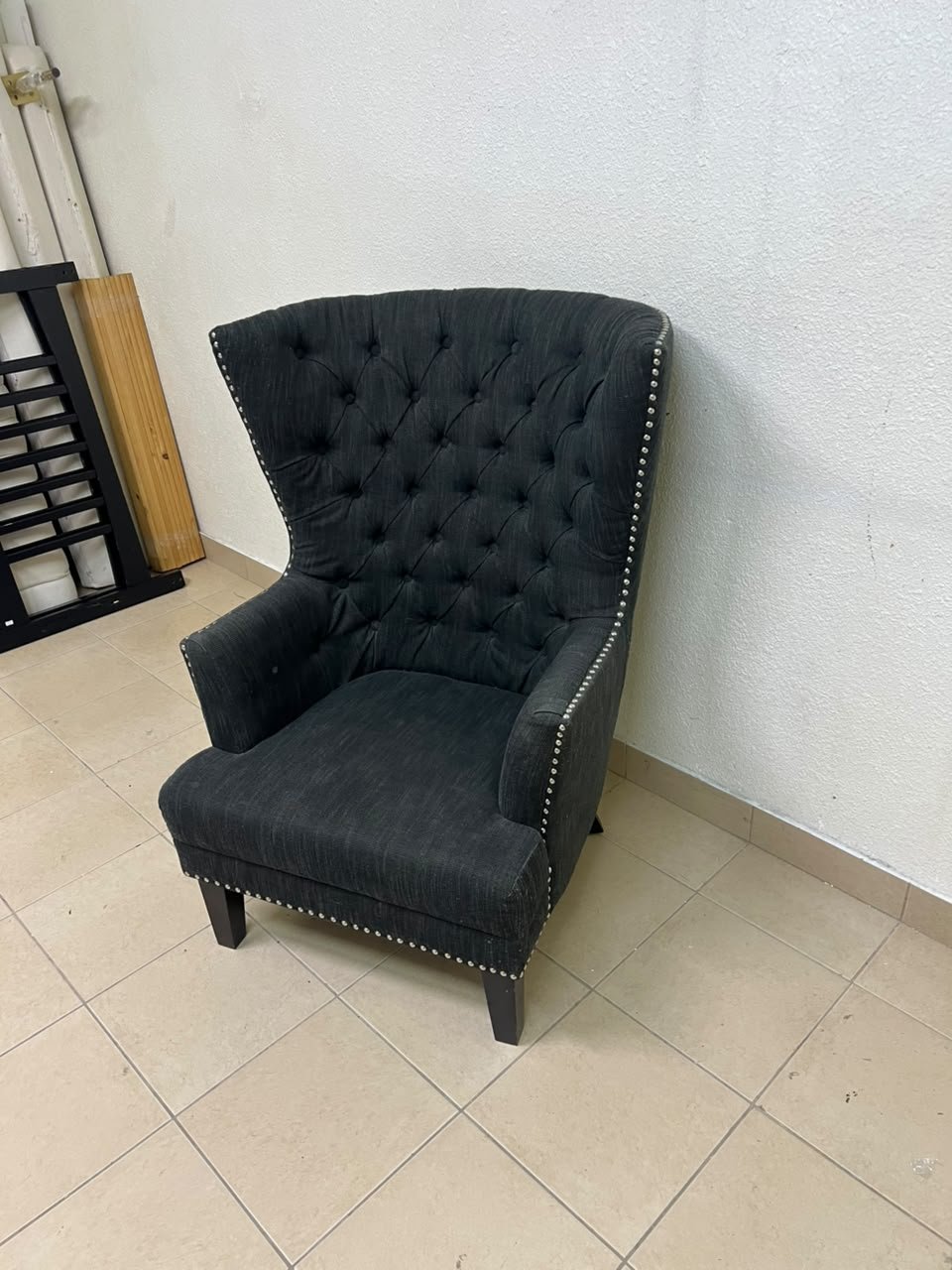 A single upholstered wingback chair featuring a button-tufted back, a black or dark gray fabric finish, and metal nailhead trim along the edges. - Image 6