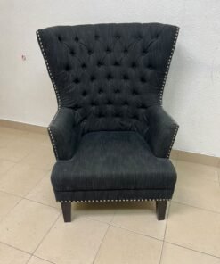 A single upholstered wingback chair featuring a button-tufted back, a black or dark gray fabric finish, and metal nailhead trim along the edges. - Image 12