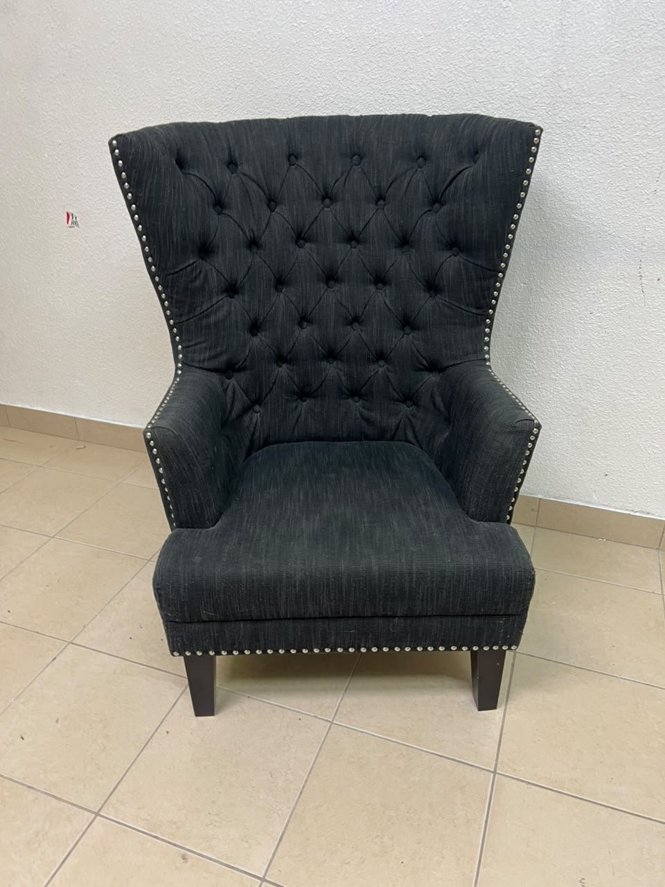 A single upholstered wingback chair featuring a button-tufted back, a black or dark gray fabric finish, and metal nailhead trim along the edges. - Image 12