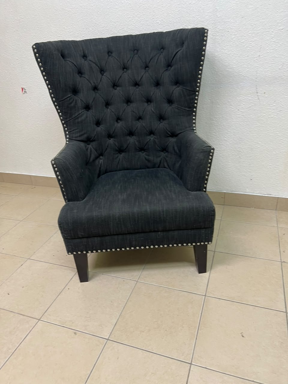 A single upholstered wingback chair featuring a button-tufted back, a black or dark gray fabric finish, and metal nailhead trim along the edges. - Image 11