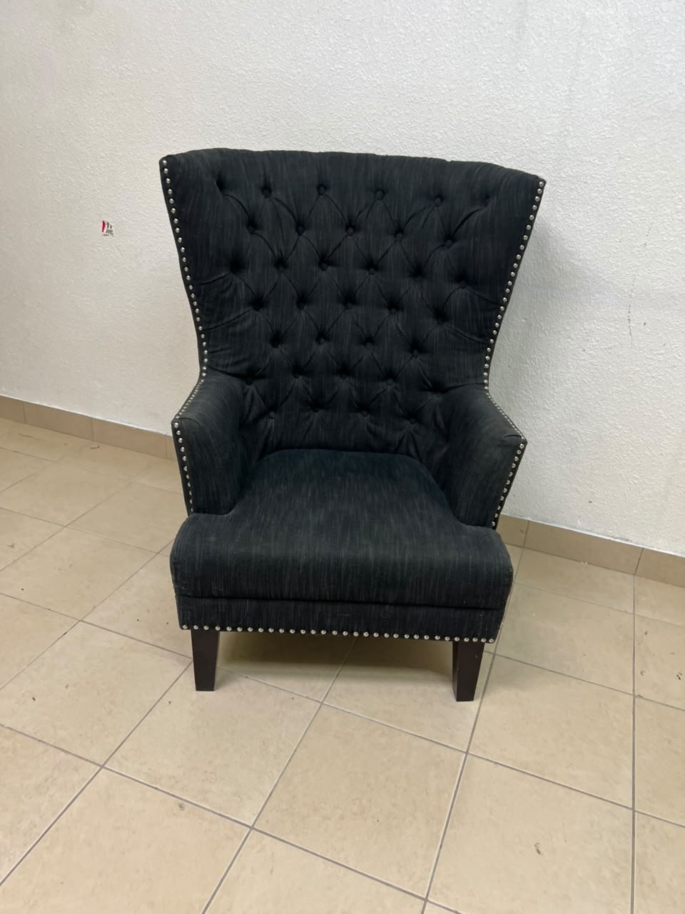 A single upholstered wingback chair featuring a button-tufted back, a black or dark gray fabric finish, and metal nailhead trim along the edges. - Image 8
