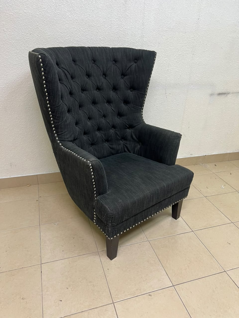 A single upholstered wingback chair featuring a button-tufted back, a black or dark gray fabric finish, and metal nailhead trim along the edges. - Image 7