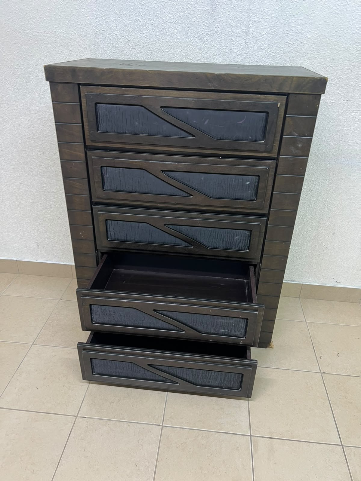 A tall, 5-drawer wooden chest featuring a dark walnut finish and a front design with raised geometric patterns.
