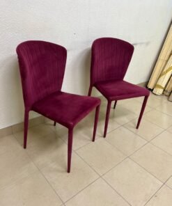 A pair of burgundy velvet dining chairs featuring a vertically ribbed backrest, sturdy metal legs, and an armless design.