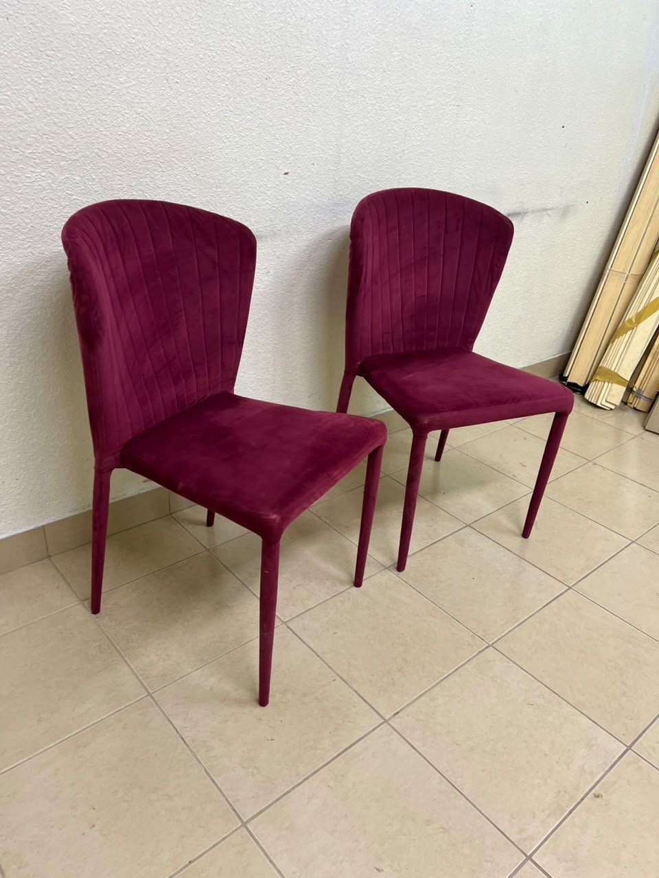 A pair of burgundy velvet dining chairs featuring a vertically ribbed backrest, sturdy metal legs, and an armless design.