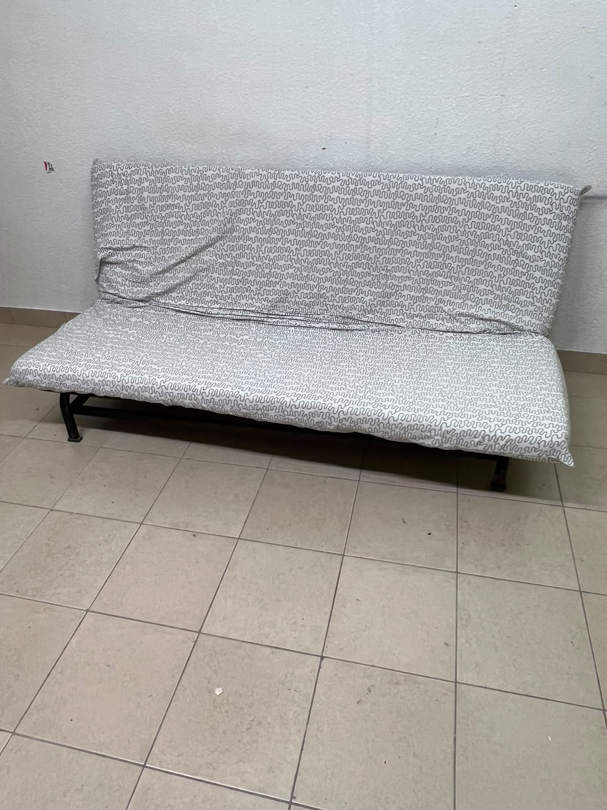 A foldable metal sofa bed (converting into a bed)—the famous IKEA NYHAMN model—featuring a grey-and-white patterned fabric cover and a black frame.