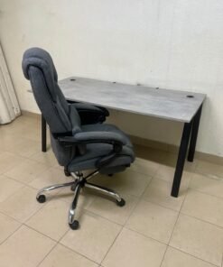 A modern office desk featuring a wooden top with a grey cement-effect finish and black metal legs, accompanied by a suspended side drawer unit in black and white, and a high-back swivel office chair upholstered in grey fabric.