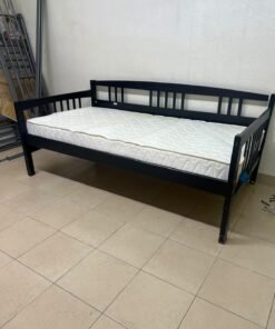 The image appears to show a dark black wooden daybed, featuring rails on three sides and a standard double size with a white mattress.