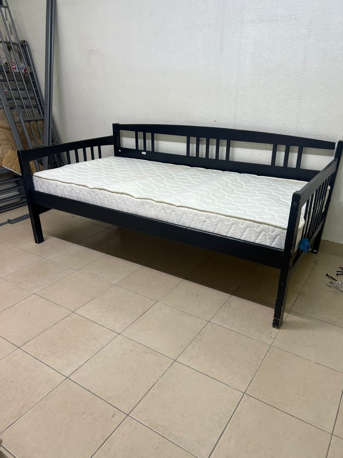 The image appears to show a dark black wooden daybed, featuring rails on three sides and a standard double size with a white mattress.