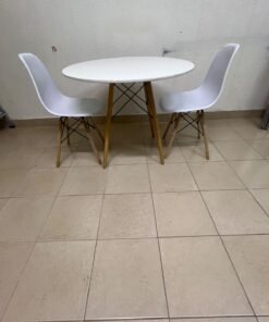 A modern Scandinavian-style round white dining table with wooden legs, accompanied by two matching white chairs.