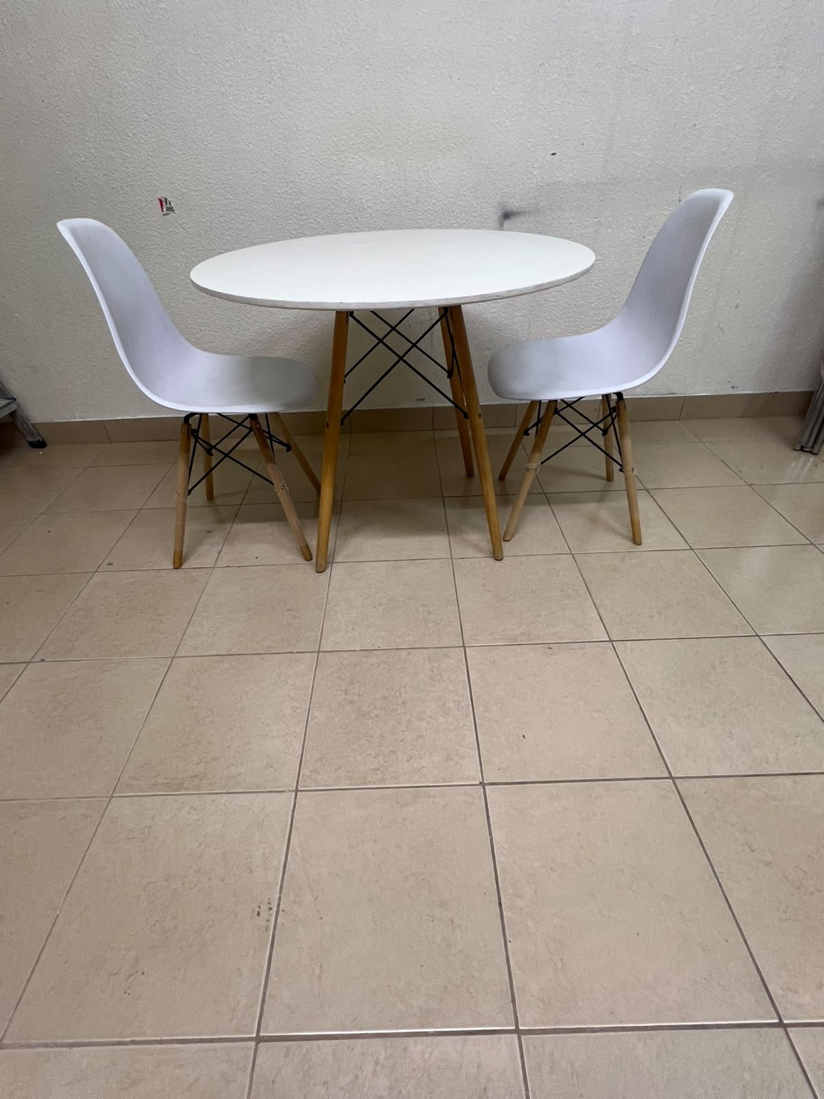 A modern Scandinavian-style round white dining table with wooden legs, accompanied by two matching white chairs.