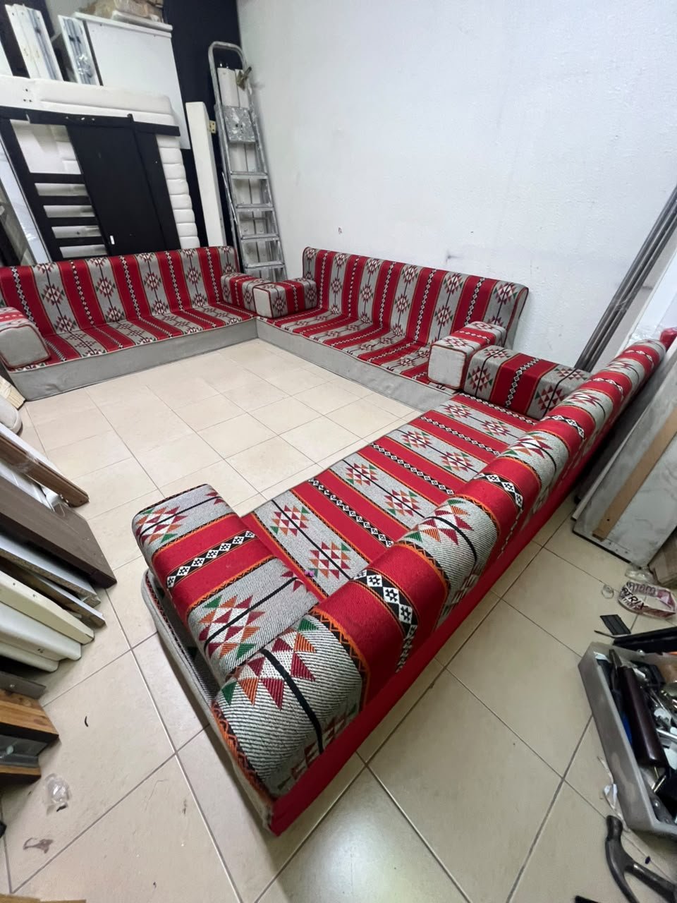 A traditional U-shaped floor seating set (Arabic *majlis*), upholstered in fabric featuring red, heritage-inspired Sadu patterns.