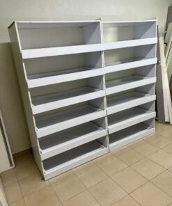 Commercial display shelving units—or slanted racks for organizing shoes or products—made of wood or white MDF. Each unit features several horizontal or slightly inclined shelves equipped with front edges to prevent products from falling.