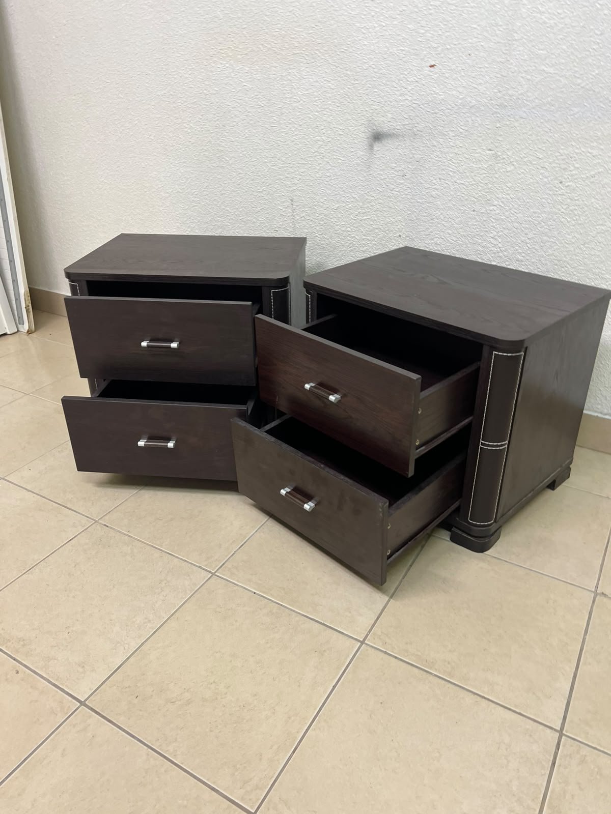 Two dark brown wooden bedside tables (nightstands) featuring two drawers and curved corners, accented with contrasting white stitching and silver-colored metal drawer handles. - Image 3