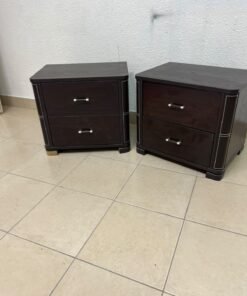 Two dark brown wooden bedside tables (nightstands) featuring two drawers and curved corners, accented with contrasting white stitching and silver-colored metal drawer handles.