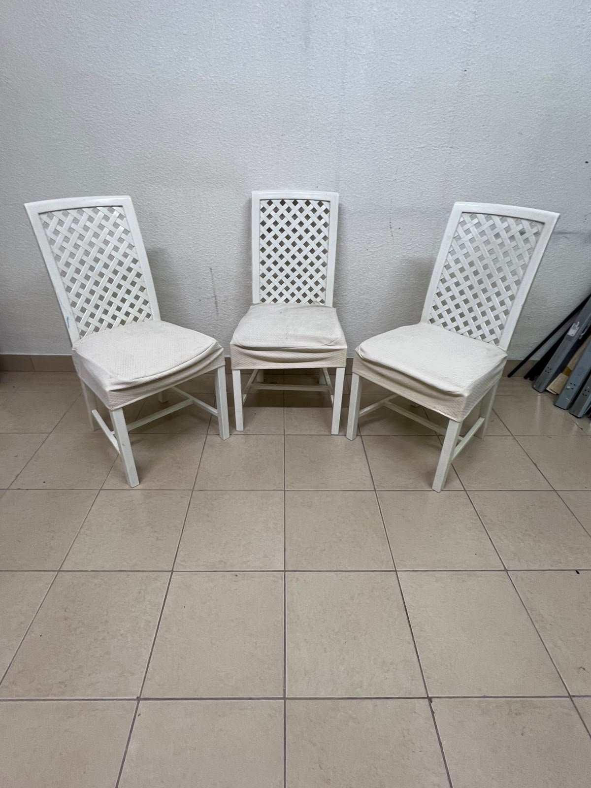 A set of white wooden chairs featuring a woven-mesh backrest design and white seat covers.